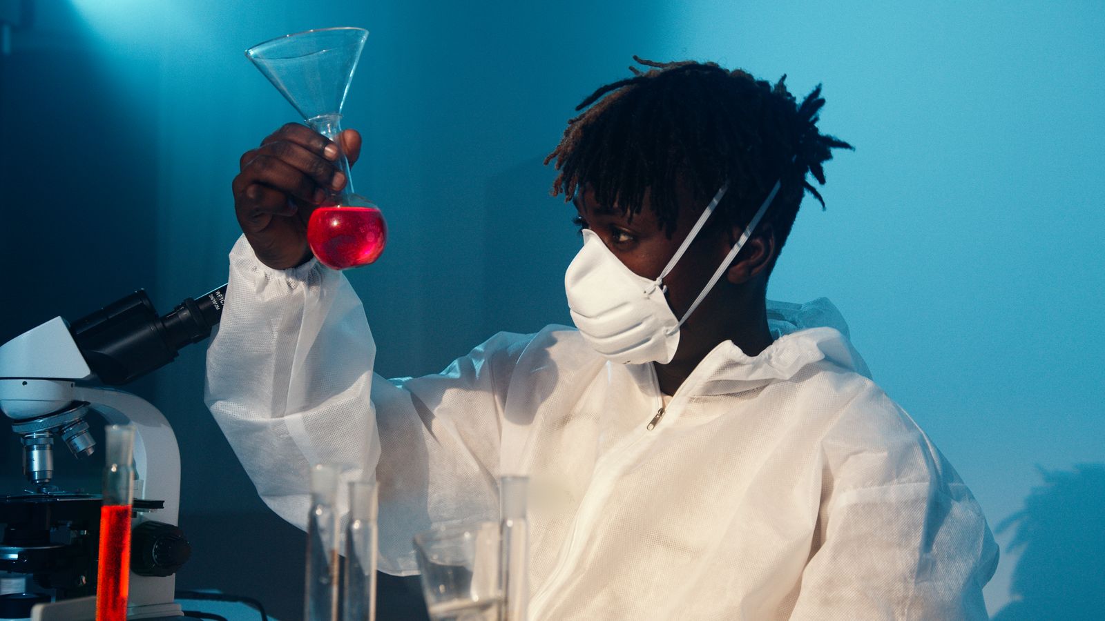 Un scientifique en combinaison de protection examine un produit chimique rouge dans un laboratoire.